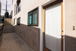 Un edificio con una porta bianca contrassegnata dalla lettera 'E', una scalinata che conduce a un pianerottolo e una finestra con persiane.