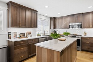 A modern kitchen with dark wood cabinets, stainless steel appliances, and a central island with plants.