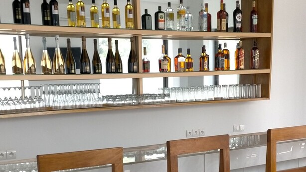 A bar area with three wooden bar stools and a shelf displaying various bottles. - MARBELLA HOTEL (Lomé)