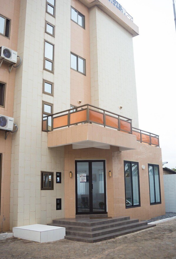 Een modern gebouw met een platte gevel, grote ramen en een balkon met oranje leuningen.