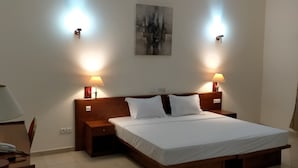 A hotel room with a wooden bed, two bedside lamps, a bedside table with a lamp, and a painting on the wall. - MARBELLA HOTEL (Lomé)
