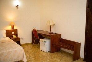 Een kleine hotelkamer met een bed, een bureau, een stoel, een lamp en een koelkast.