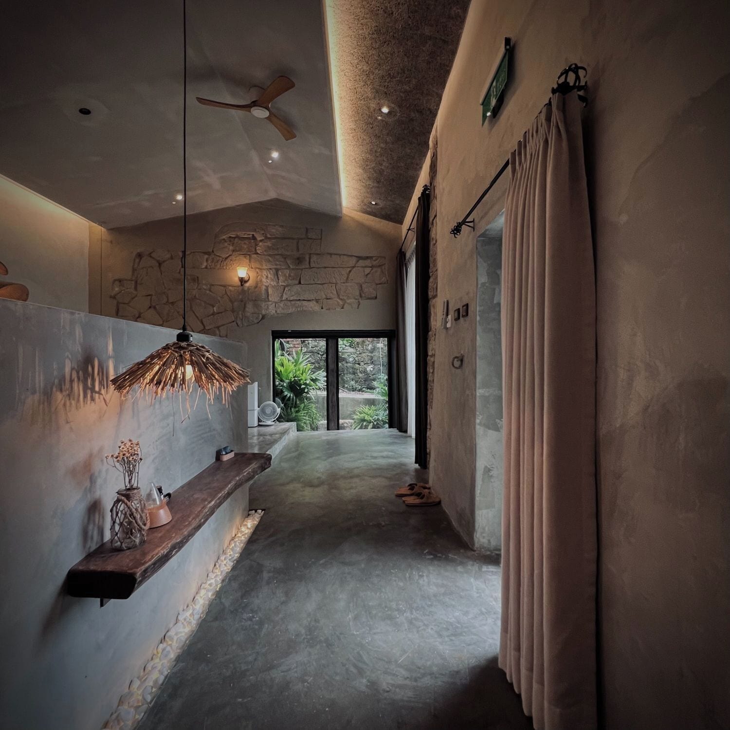 Ein modernes Interieur mit Steinwand, Pendelleuchte und Blick durch eine Glastür.