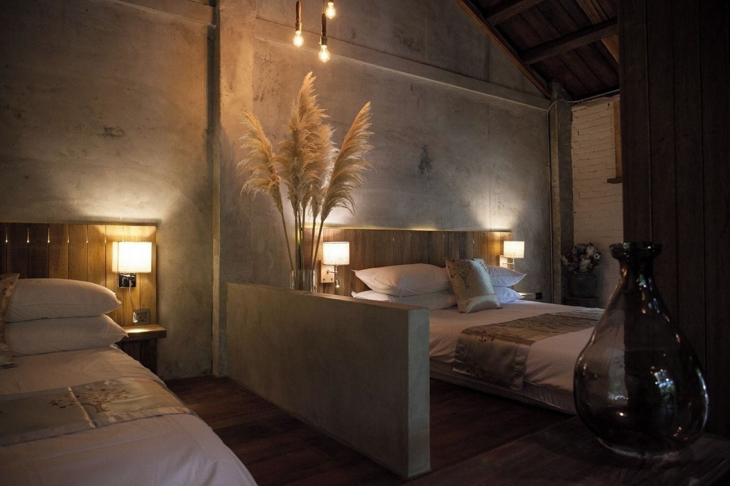 A bedroom with a wooden headboard, bedside lamps, a nightstand, a large vase, and a bed with white linens.