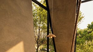 A modern interior with a hanging chair, a wicker basket with plants, a vintage radio, and a view of greenery outside. - Twilight Forest (New Taipei City)