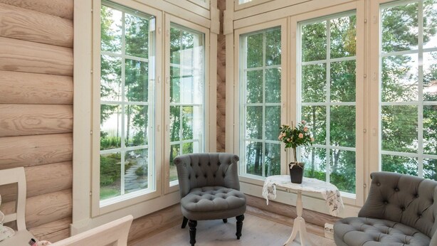 A room with large windows, a grey upholstered armchair, a small table with a vase of flowers, and a wooden floor. - Torniniemi by Interhome (Punkaharju)