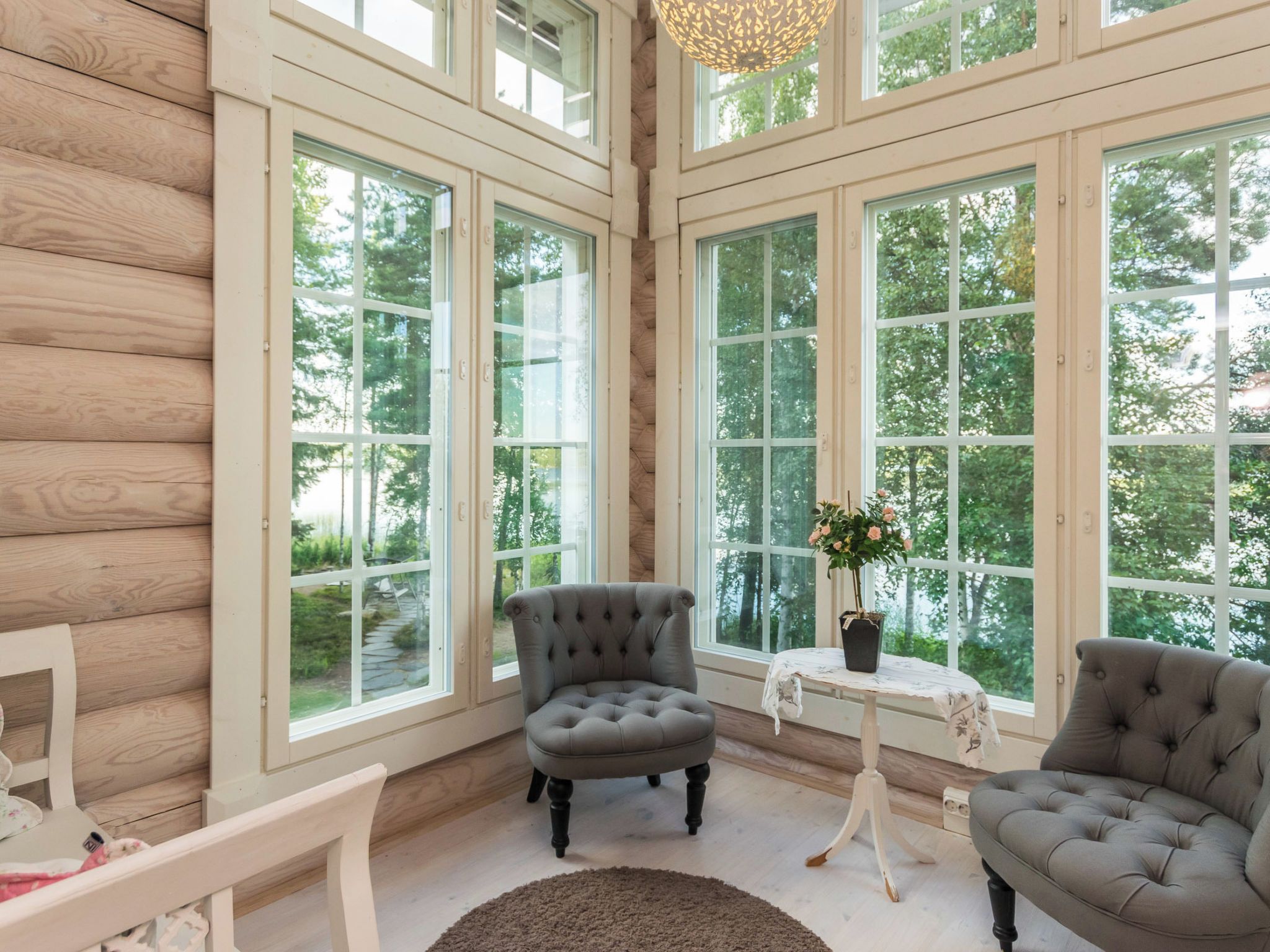 Une pièce dotée de grandes fenêtres, d’un fauteuil capitonné, d’une petite table sur laquelle est posée une plante en pot et d’un plancher en bois.