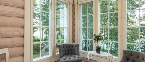 A room with large windows, a tufted armchair, a small table with a potted plant, and a wooden floor.