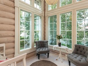 Una habitación con ventanas amplias, un sillón capitoné, una mesita con planta en maceta y suelo de madera.