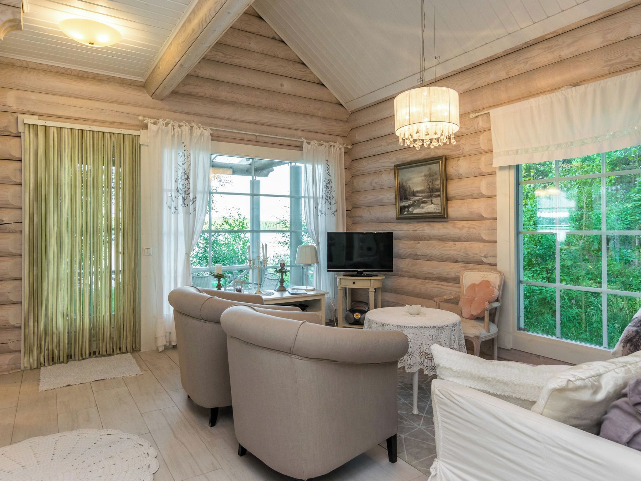 A cozy room with a television, two sofas, a table, and a large window with a view of greenery.