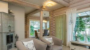 A cozy log cabin interior with a fireplace, two armchairs, a round table, and large windows offering a view of greenery. - Torniniemi by Interhome (Punkaharju)