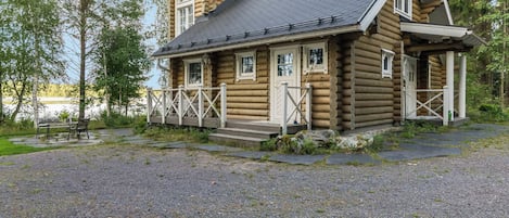 A log cabin with a porch, a chimney, and a view of a lake.