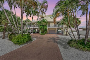 A beachfront property with a two-story house, a covered driveway, and a sandy beach area. - Dolphin Tales: Pool, Bay Views & Private Beach by Anna Maria Life Vacation Rentals (Anna Maria)