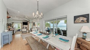 Ein geräumiger Essbereich mit einem großen Tisch, gedeckt für sechs Personen, einem Chandelier und Meerblick durch große Fenster.