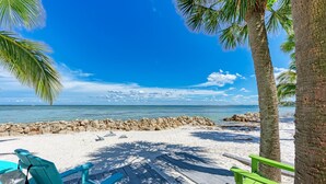 Ein Strand mit weißem Sand, einer Holzterrasse und türkisfarbenen Stühlen.