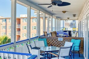 Una terrazza esterna con tavoli e sedie, una ventola a soffitto e vista su un edificio con balconi.