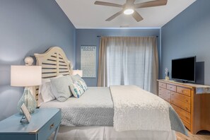 Une chambre à coucher comprenant un lit, une table de chevet, une commode, un téléviseur et un ventilateur de plafond.