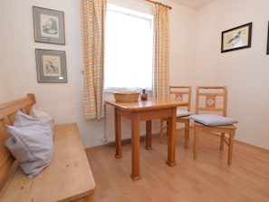 Una habitación con un banco de madera, una mesa con una cesta, dos sillas y dos cuadros en la pared.