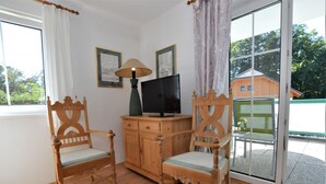 Ein Zimmer mit zwei Holzstühlen, einem Fernseher auf einer Holzkommode und einem großen Fenster mit Vorhängen.