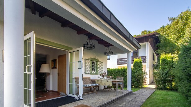 Ein modernes Haus mit überdachter Veranda, Essbereich und gepflegtem Garten.