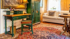 Ein traditionell eingerichteter Raum mit einem grünen Schreibtisch, einem gemusterten Teppich, einem weißen Sofa und einer Kristallleuchter.