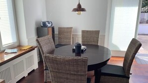 Un comedor con una mesa redonda, sillas de mimbre, una lámpara colgante y una ventana con persianas.