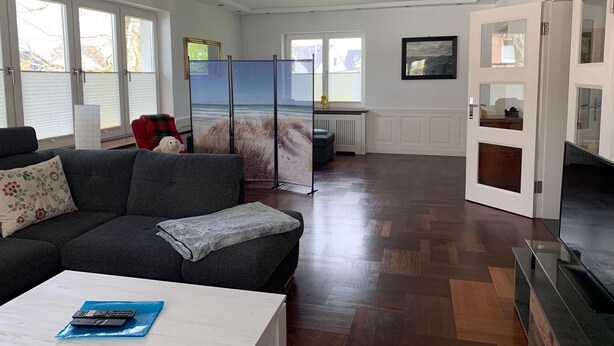 Un salón amplio con un sofá gris, una mesa de centro blanca y un mueble para la televisión.