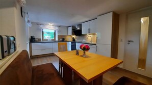 A modern kitchen with white cabinets, a wooden dining table, and a built-in oven.