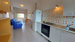 Eine kompakte Küche mit weißen Schränken, einem Gasherd und einem Kühlschrank. Es gibt einen Essbereich mit Tisch und Stühlen sowie ein blaues Sofa im Wohnbereich.