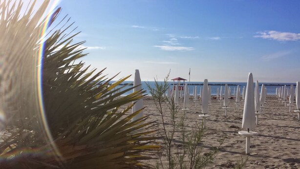 Ein Strand mit weißen Sonnenschirmen und einem Gebäude mit rotem Dach in der Ferne.
