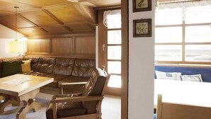 Una habitación con techo de madera, un sofá de cuero marrón, una mesa de madera y una ventana con persianas.