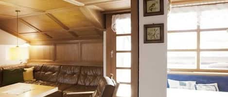 Ein Zimmer mit Holzboden, einem braunen Ledersofa, einem Holztisch und einem Fenster mit Jalousien.