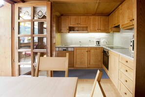 Interior de madera con cocina, comedor y vista a través de un ventanal.