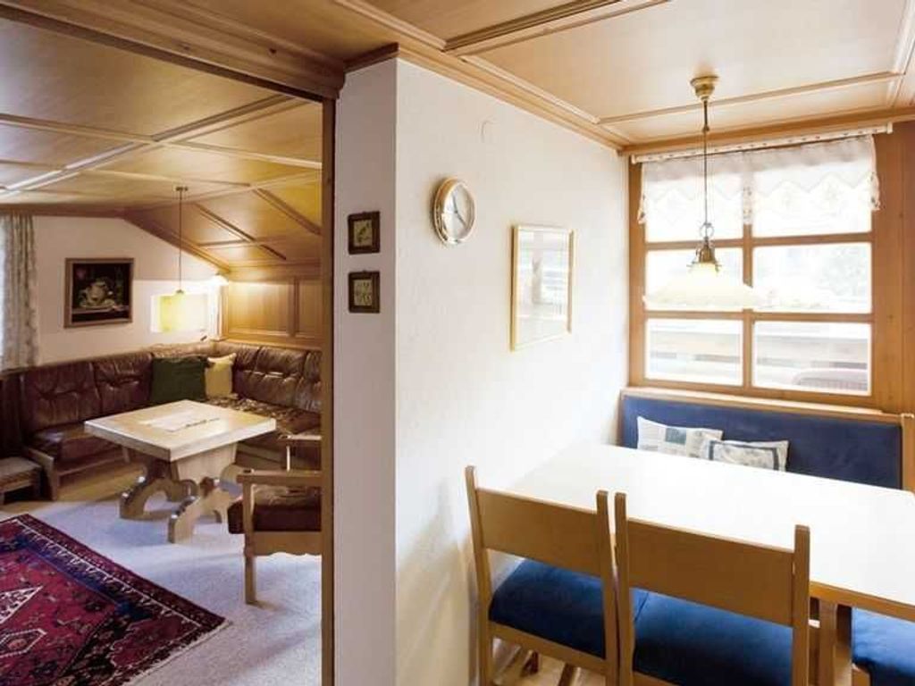 A room with a dining table, chairs, a sofa, a window with curtains, and a clock on the wall.