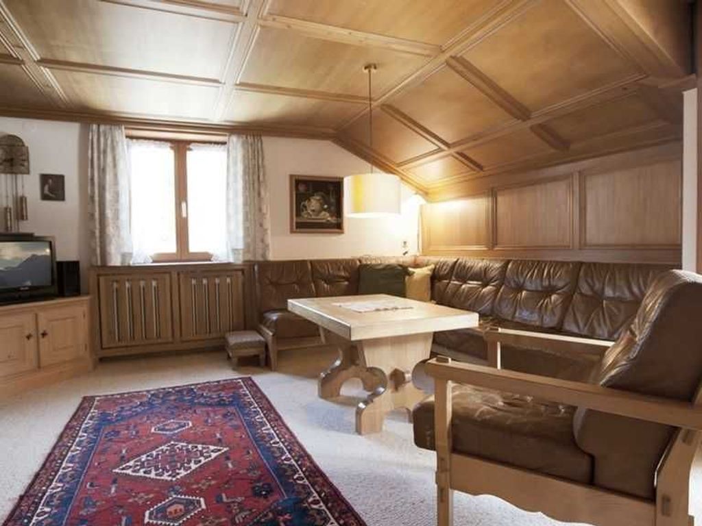 Een kamer met een houten plafond, een bank, een tafel en een kamerbreed tapijt met een patroon.