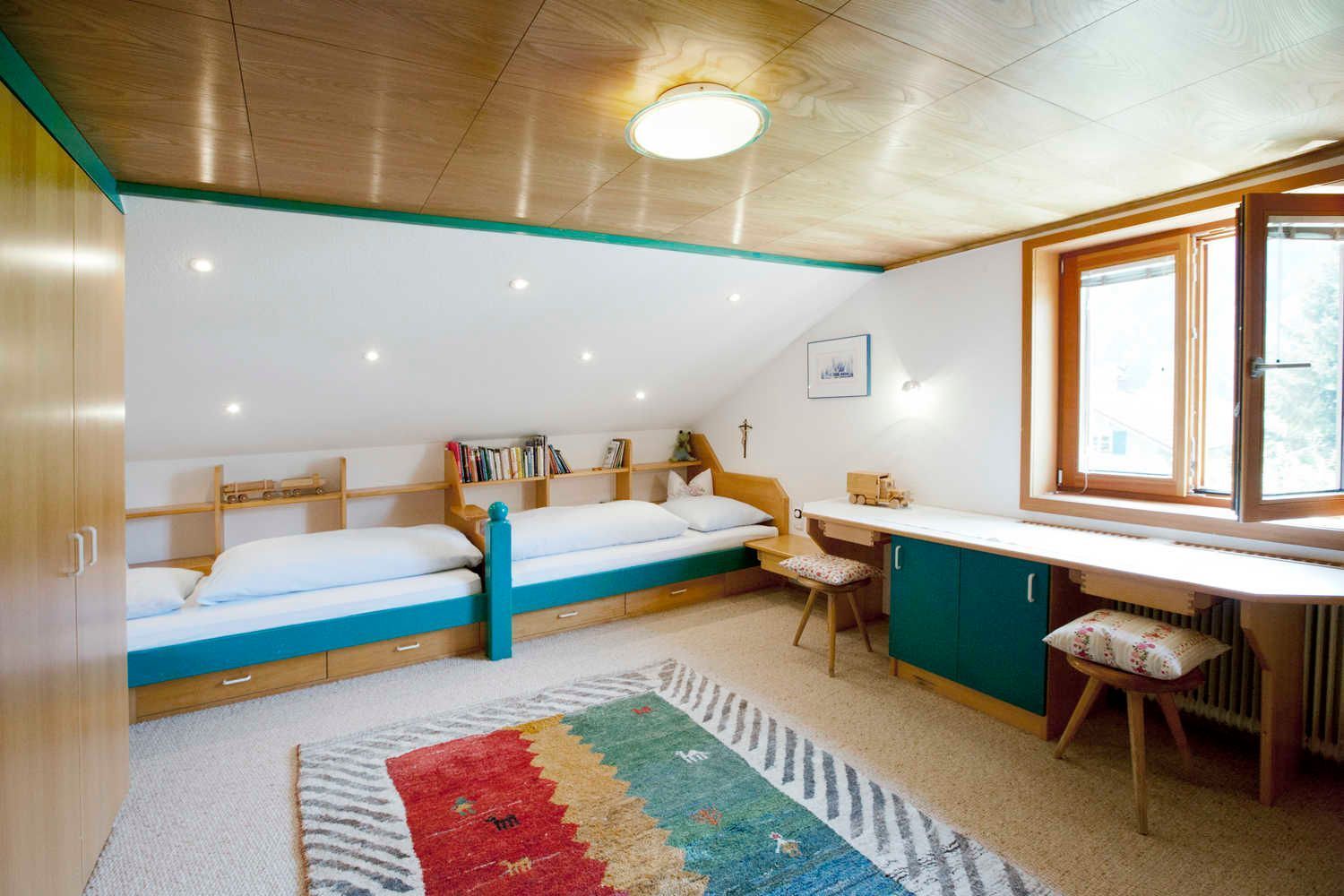 A room with bunk beds, a desk, a chair, and a window.