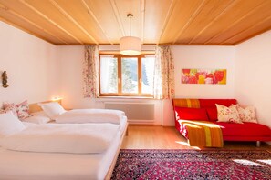 Une chambre à coucher avec un lit, un canapé rouge, une fenêtre avec des rideaux, un radiateur et un tableau accroché au mur.