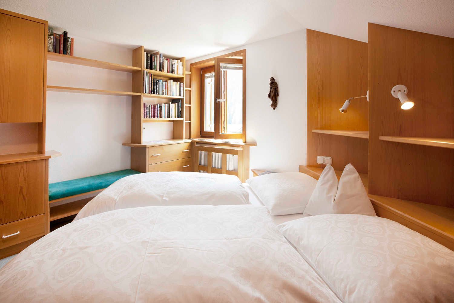 Une chambre avec deux lits, une bibliothèque en bois, un bureau et une fenêtre.