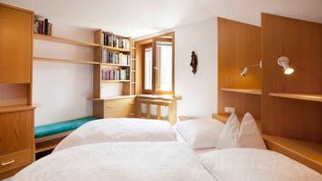 Une chambre avec deux lits, une bibliothèque en bois, un bureau et une fenêtre.