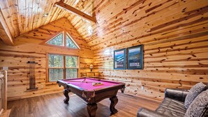 A wooden interior with a pool table, a sofa, and framed pictures on the wall. - Summer Offer • 5 King Suites • Games • Pool Access (Sevierville)