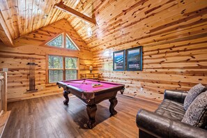 Relax in a rustic retreat with a pool table, leather couch, and framed pictures on the walls.