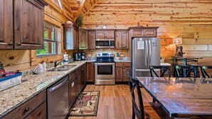 A wooden cabin-style kitchen with granite countertops, stainless steel appliances, and a dining area with a table and chairs. - Summer Offer • 5 King Suites • Games • Pool Access (Sevierville)