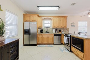Una cocina con armarios de madera, electrodomésticos de acero inoxidable, encimera de granito e iluminación en el techo.