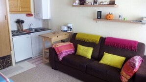 A compact living space with a kitchenette, a sofa with colorful cushions, and a small table.