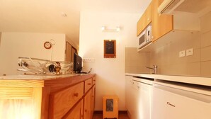 Cocina compacta con armarios de madera, un microondas y un refrigerador pequeño.