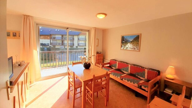 Un salón acogedor con sofá, mesa de comedor y sillas. Tiene un balcón con vistas a edificios y un cuadro en la pared.