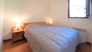 Un dormitorio con una cama individual, dos lámparas de noche, una ventana y un radiador.