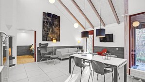 Eine moderne Küche mit Essbereich, ausgestattet mit einem großen Fenster, einer hohen Decke mit sichtbaren Balken und zeitgemäßen Möbeln.