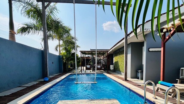 Une piscine bordée de pierres, une pergola et des palmiers.