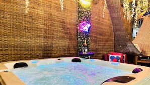 A hot tub with a textured wall backdrop, a neon sign, and a small table with a bottle and glass. - Luxury Escape w/ Infinity Pool & Hot Tub Bar (Adenta)
